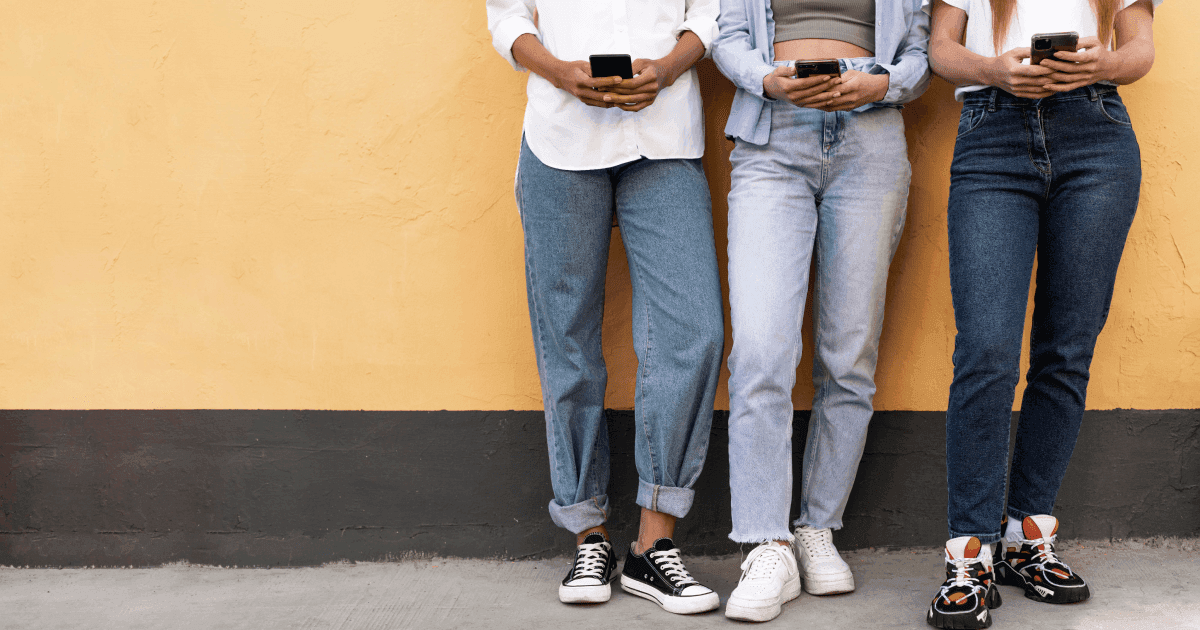 Students on their phones leaning against a yellow wall